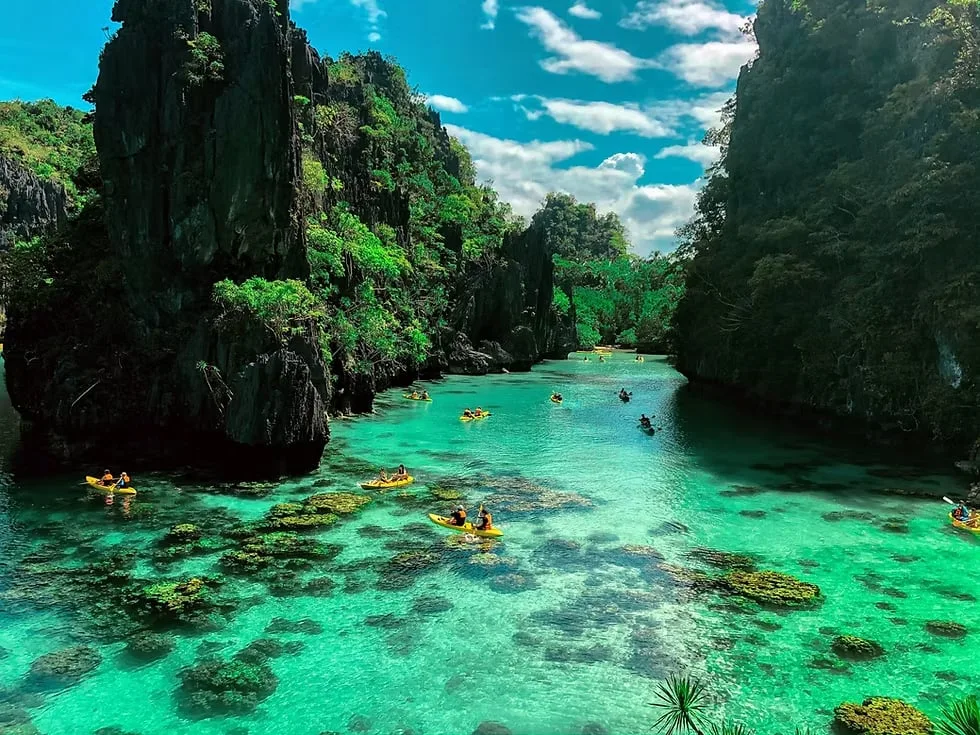 Guests kayaking over clear turquoise water into the Big Lagoon, between limestone cliffs