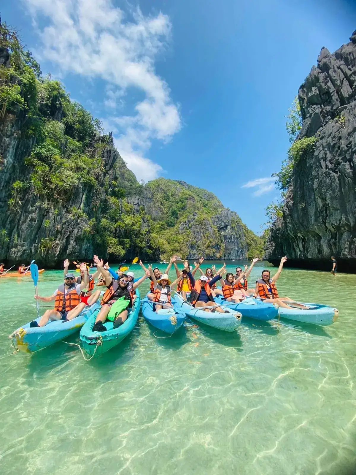 A group of Anang guests in kayaks waving in a clear lagoon between limestone cliffs