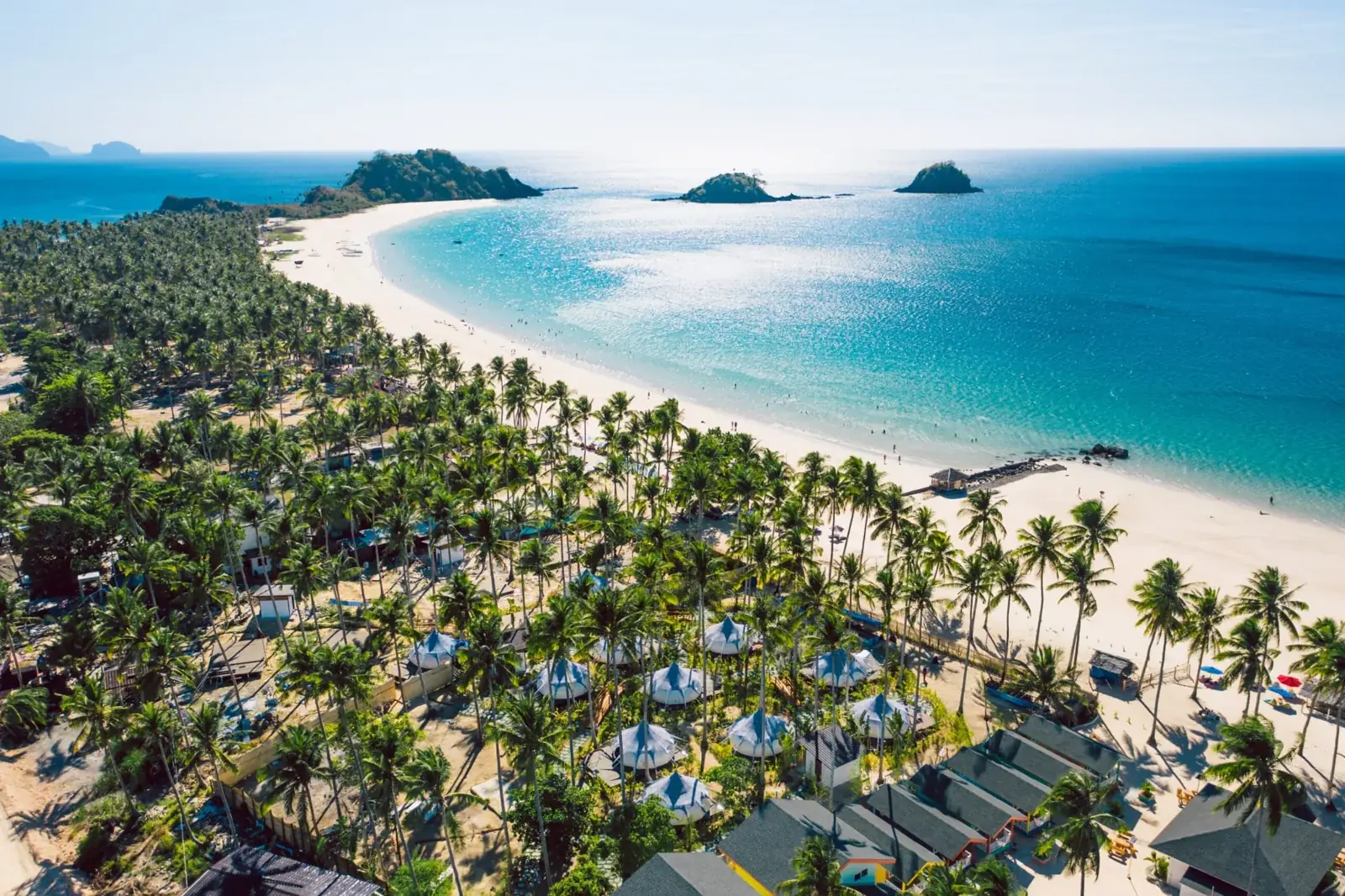 Aerial view of Nacpan Beach, a long curve of white sand lined with coconut palms