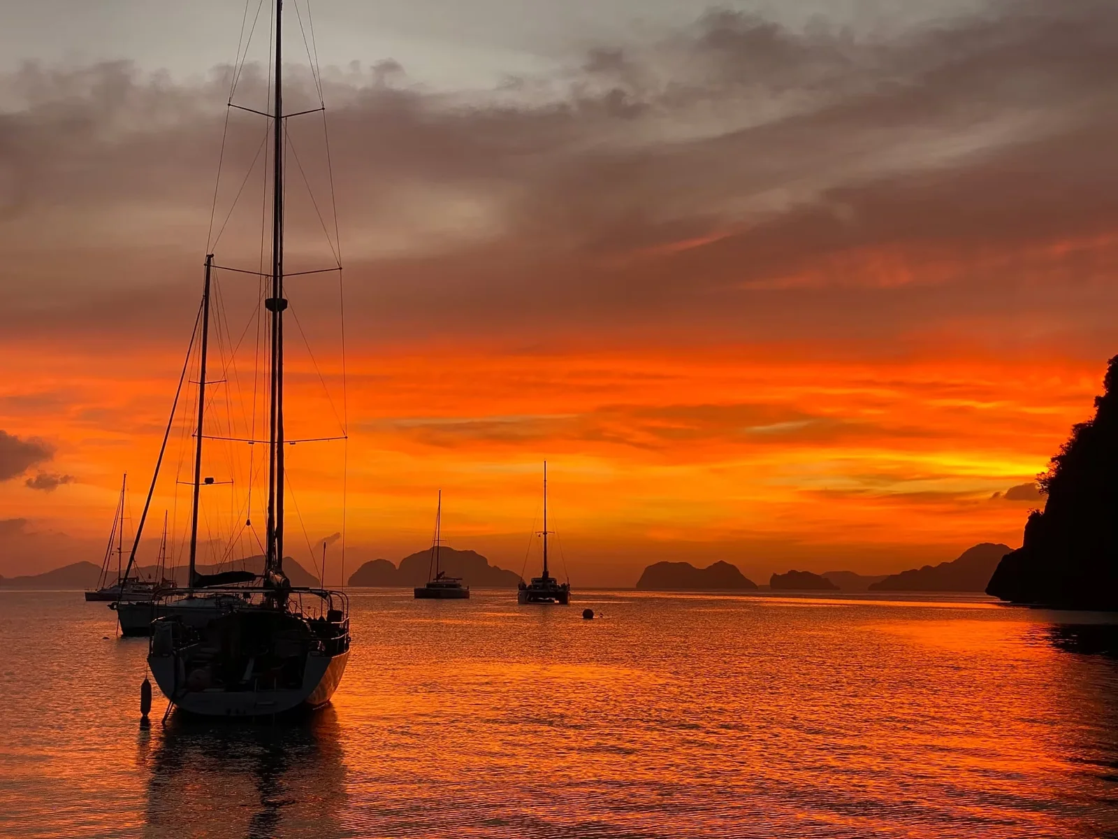 Sailboats silhouetted against a fiery orange sunset over the islands of Bacuit Bay