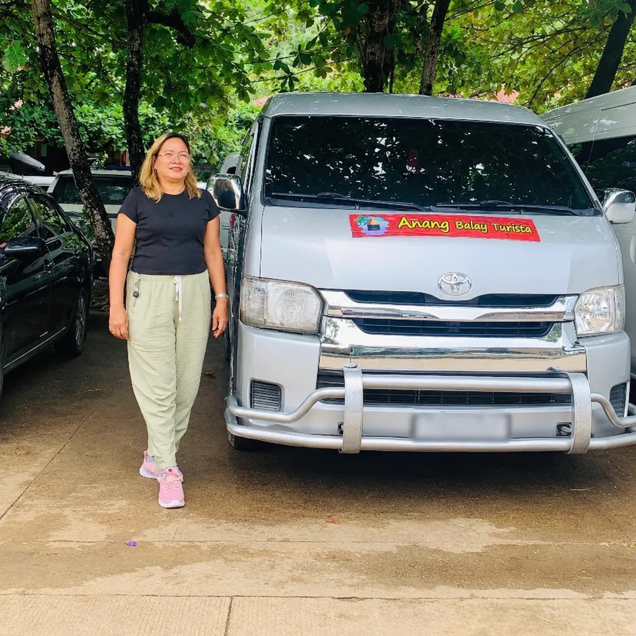 An Anang Balay Turista air-conditioned van parked under the trees, with an Anang team member beside it
